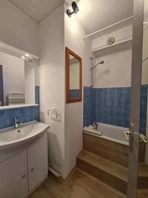 A bathroom with a sink, mirror, shower, and a wooden floor. - Ski Access Apartment w/ Mountain Views & Balcony (Saint François Longchamp)