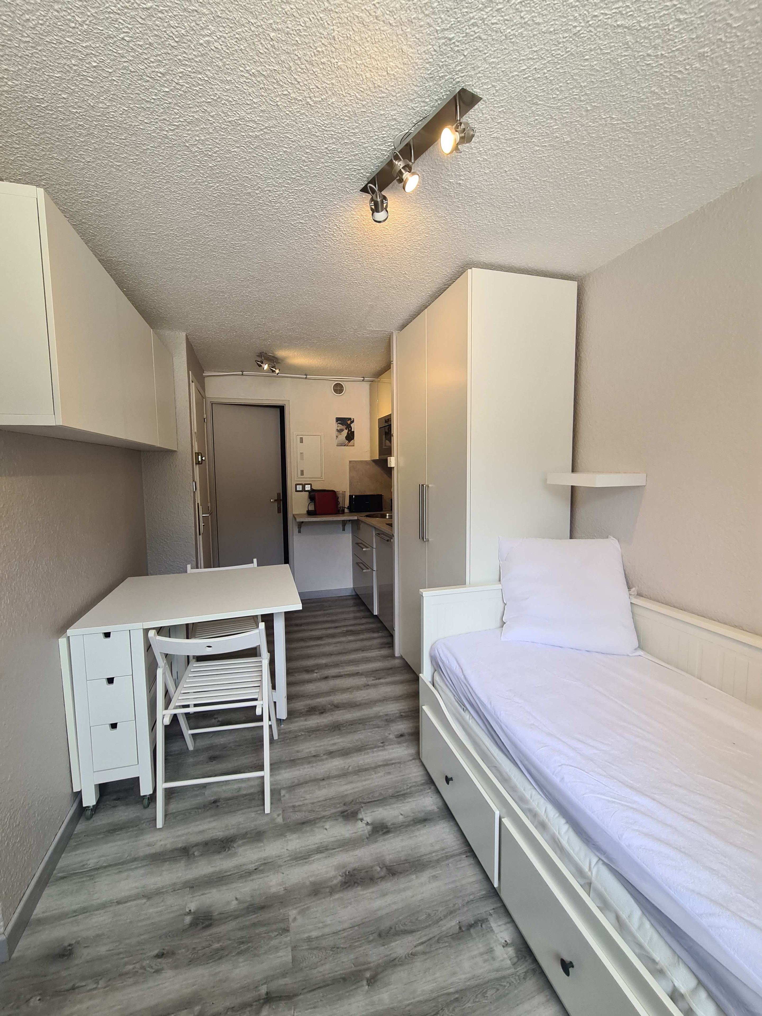 A compact room with a bed, a desk, and a kitchenette.