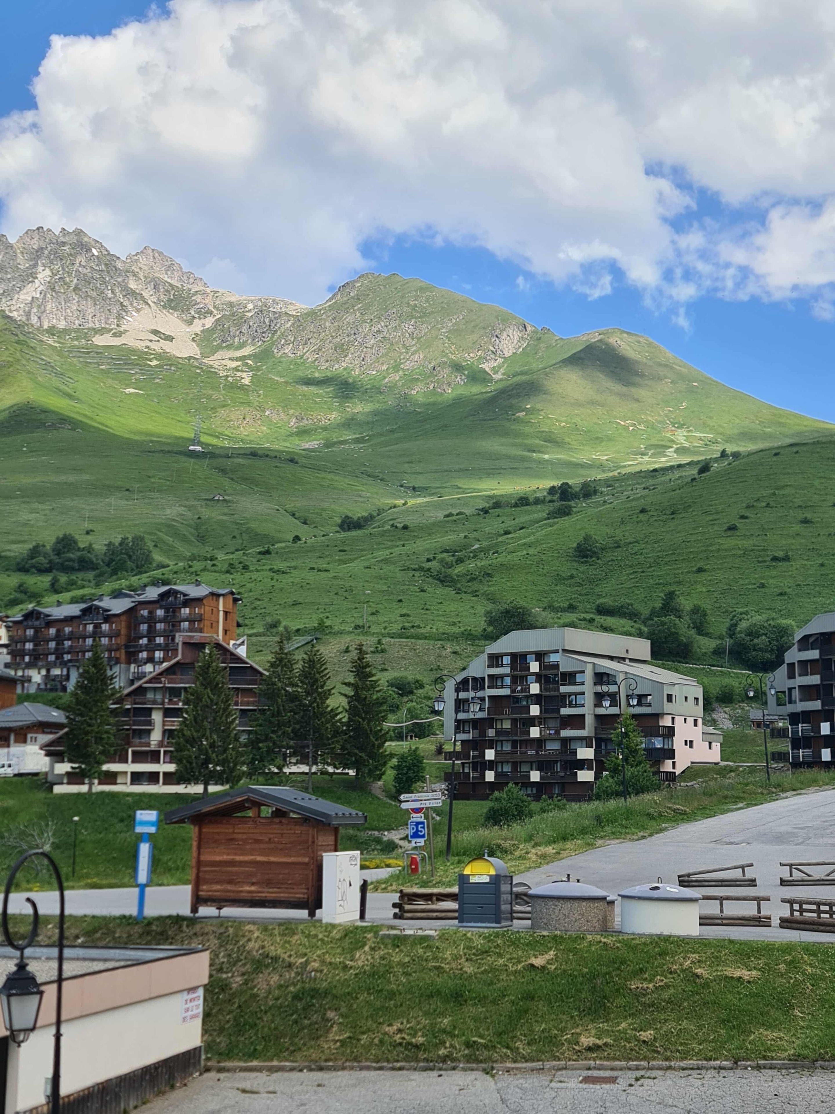 A mountainous landscape with a hotel featuring multiple floors and balconies, a parking area, and a small wooden building.