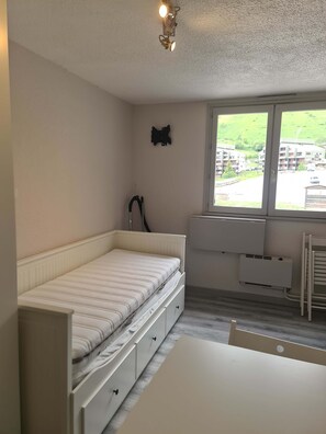Ein Schlafzimmer mit Bett, Schreibtisch, Heizkörper und Fenster mit Blick auf Gebäude.