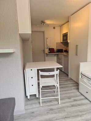 Habitación pequeña con kitchenette, un escritorio blanco y una silla.
