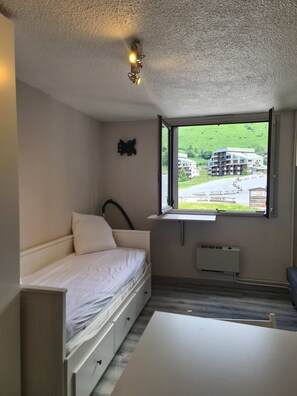 Ein Schlafzimmer mit einem Bett, einem Fenster, einer Heizung und Blick auf ein Gebäude.