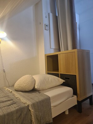 Een slaapkamer met een bed, een bedlamp, een houten kledingkast en een thermostaat op de muur.
