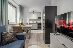 A modern living room with a sofa, a television, and a kitchen area in the background. - Lumina 3 room apart near PGE Narodowy (Warszawa)