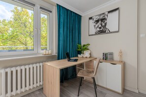 Une pièce comprenant un bureau, une chaise, un radiateur, une fenêtre, des rideaux et un tableau encadré accroché au mur.
