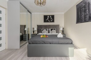Une chambre à coucher moderne avec un grand lit, des tables de chevet, un miroir et un lustre.