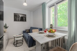A modern room with a dining table, a blue sofa, a small round table, and a window with curtains. - Lumina 3 room apart near PGE Narodowy (Warszawa)