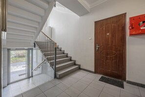 A staircase with a glass door leading outside, a wooden door with a handle, and a red fire alarm box on the wall. - Lumina 3 room apart near PGE Narodowy (Warszawa)