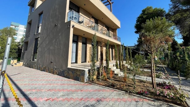 A modern two-story building with balconies, a paved entrance area, and a garden with various plants. - Room-sea Pearl Studios Golem - Ground-fl (Golem)