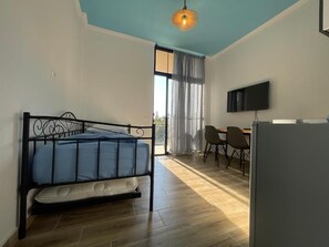 A room with a bed, a desk, a chair, a television, and a window with curtains. - Room-sea Pearl Studios Golem - Ground-fl (Golem)