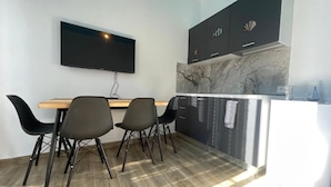 A modern kitchen with a marble backsplash, a flat-screen TV mounted above the counter, and a dining area with four chairs. - Room-sea Pearl Studios Golem - Ground-fl (Golem)