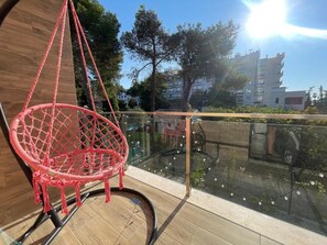 A red hanging chair on a balcony with a glass railing, overlooking a residential area with trees and buildings. - Room-sea Pearl Studios Golem - Ground-fl (Golem)