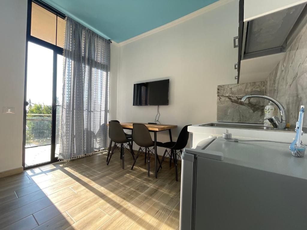 A modern kitchen with a flat-screen TV, a dining area with chairs, and a large window with curtains.