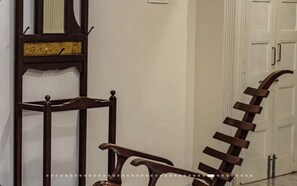 Un pasillo con una silla de madera y una escalera metálica apoyada en la pared.
