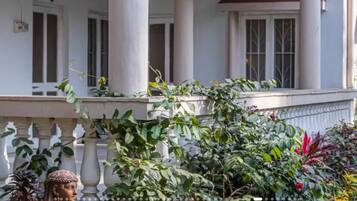 A building with a white facade, columns, and a balcony with plants.