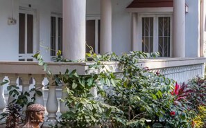 Un edificio de fachada blanca, con columnas y un balcón lleno de plantas.