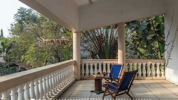 Ein überdachter Balkon mit Tisch und Stühlen, umgeben von einem weißen Geländer und üppiger Vegetation.