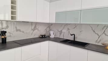 A modern kitchen with white cabinets, a marble backsplash, a black countertop, and a sink.