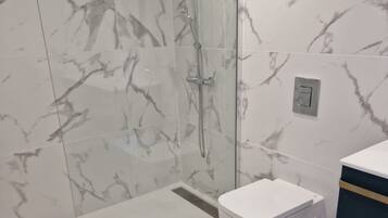A modern bathroom with a glass shower enclosure, a white toilet, and a wooden floor.