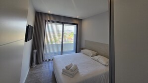 A modern hotel room with a large bed, a flat-screen TV mounted on the wall, and a view of the outdoors through the window. - Ocean Paradise Santa Luzia (Funchal)
