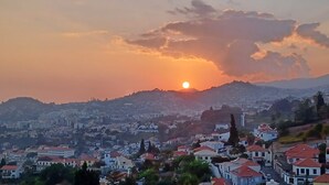 A cityscape with a sunset over a hill, featuring residential buildings with red roofs. - Ocean Paradise Santa Luzia (Funchal)