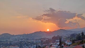 A cityscape with a sunset over a hill, featuring residential buildings with red roofs.