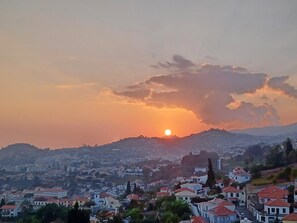 A cityscape with a sunset over a hill, featuring residential buildings with red roofs. - Ocean Paradise Santa Luzia (Funchal)