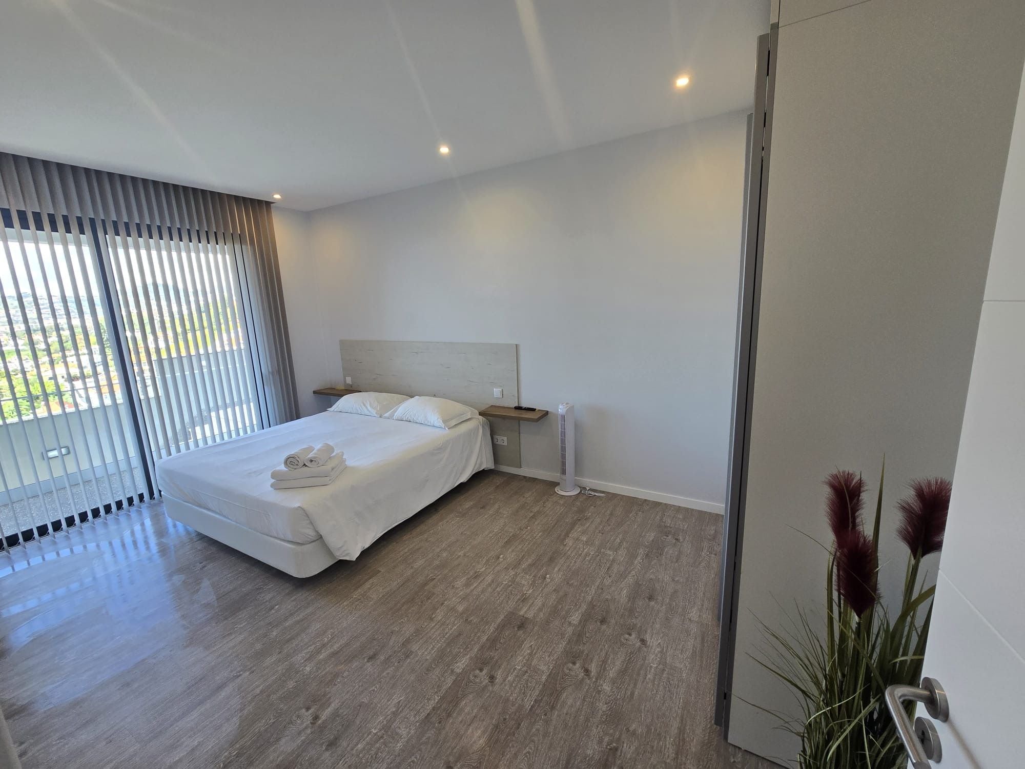 A modern bedroom with a bed, bedside table, and a view through the window.