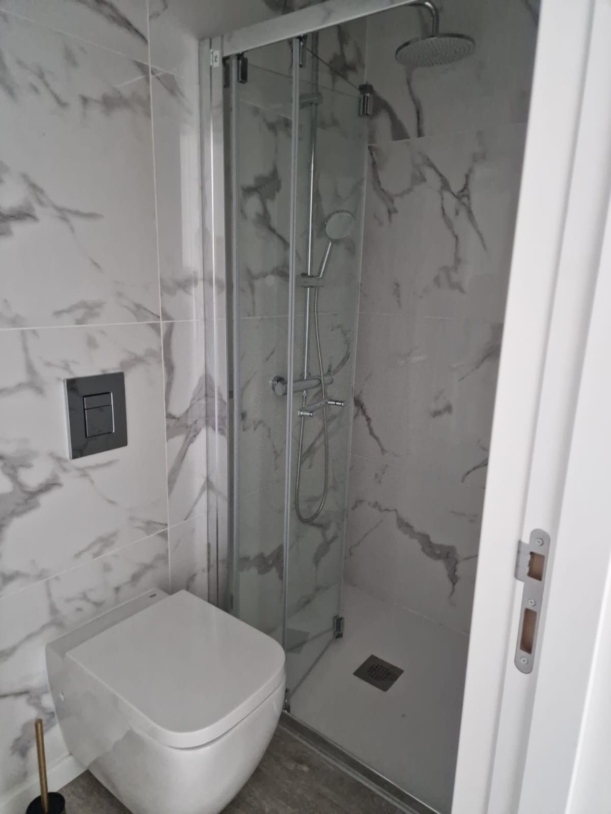 A bathroom with a glass-enclosed shower, a white toilet, and marble-patterned walls.