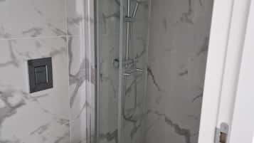 A bathroom with a glass-enclosed shower, a white toilet, and marble-patterned walls.
