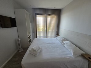 Ein Hotelzimmer mit einem Bett, einem an der Wand befestigten Fernseher und einem Fenster mit Jalousien.
