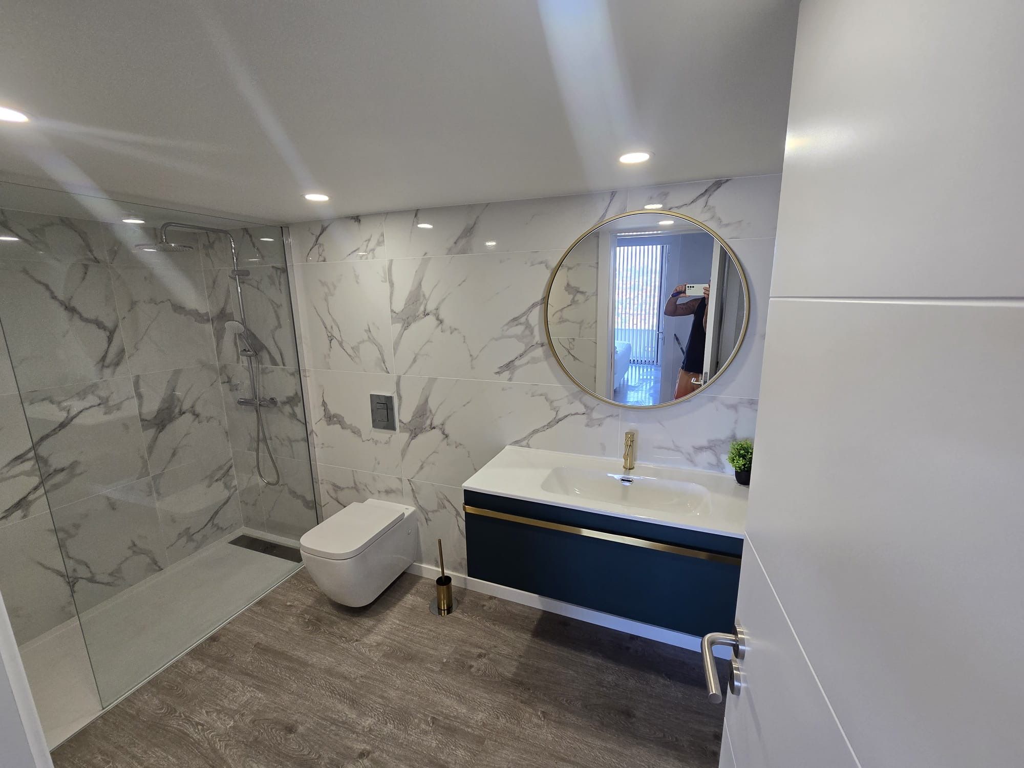 Een moderne badkamer met een marmeren wand, een ronde spiegel, een wastafel en een toilet.