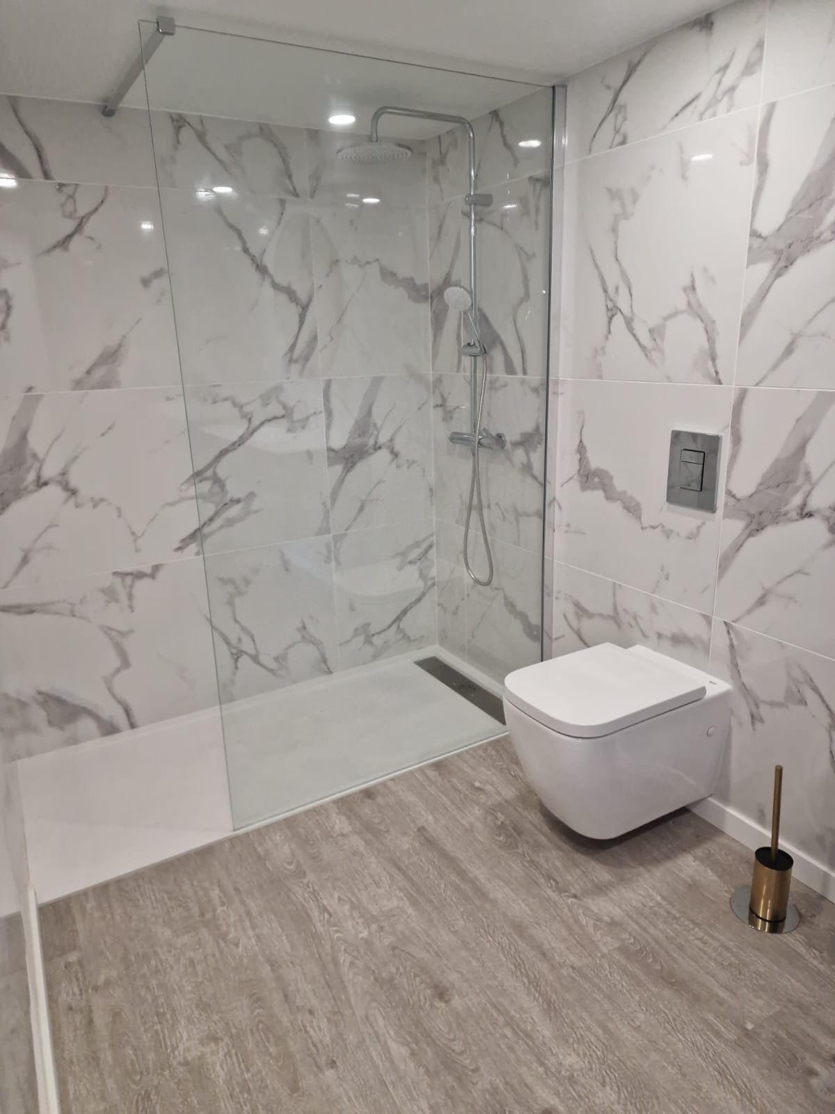A modern bathroom with a glass-enclosed shower, a white toilet, and marble-patterned walls.