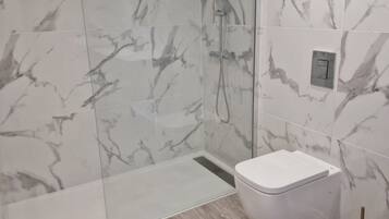 A modern bathroom with a glass-enclosed shower, a white toilet, and marble-patterned walls.