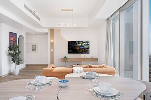 Un salon moderne avec un grand téléviseur à écran plat fixé au mur, un canapé, une table à manger pour quatre personnes et une plante en pot.