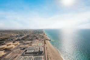 An aerial view of a coastal industrial area with storage tanks, solar panels, and a beach. - Ocean & Palm Views / Infinity pool / High floor (Dubai)