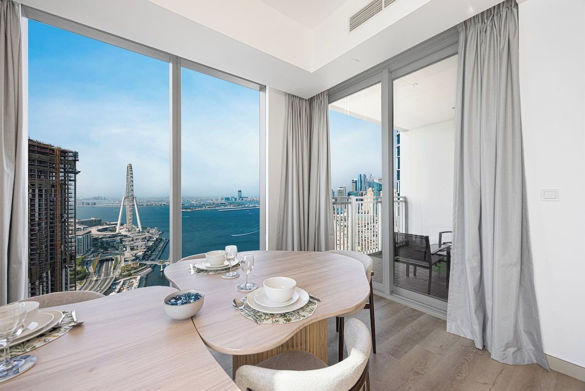 A modern dining area with a panoramic city view, a balcony with a view, and a dining table set with plates, bowls, and glasses.
