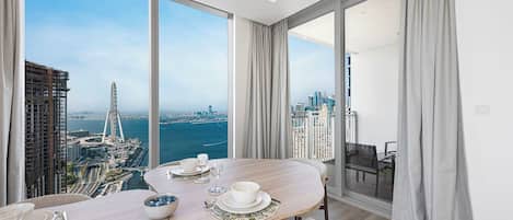 A modern dining area with a panoramic city view, a balcony with a view, and a dining table set with plates, bowls, and glasses.