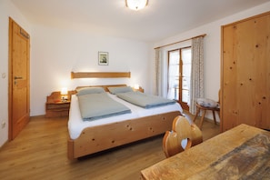 A bedroom with a wooden bed, a nightstand, a chair, and a table. - Vacation rental with a rooftop terrace and mountain views. Perfect for the Zugspitze and Eibsee. (Grainau)
