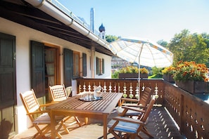 A wooden deck with a table and chairs, a decorative umbrella, and a view of a church with a dome. - Vacation rental with a rooftop terrace and mountain views. Perfect for the Zugspitze and Eibsee. (Grainau)