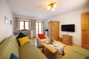 A living room with a sofa, a table with a fruit bowl, a television, and a wooden cabinet. - Vacation rental with a rooftop terrace and mountain views. Perfect for the Zugspitze and Eibsee. (Grainau)