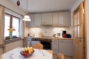 A kitchen with white cabinets, a dining table with a floral tablecloth, and a fruit bowl. - Vacation rental with a rooftop terrace and mountain views. Perfect for the Zugspitze and Eibsee. (Grainau)