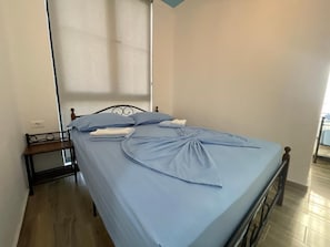 A single bed with a blue bedspread, a wooden headboard, and a bedside table with a lamp. - Room-sea Pearl Studios Golem - First-flo (Golem)
