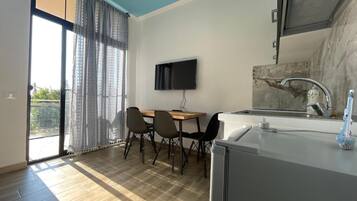 A modern kitchen with a flat-screen TV, a dining area with chairs, and a large window with curtains.
