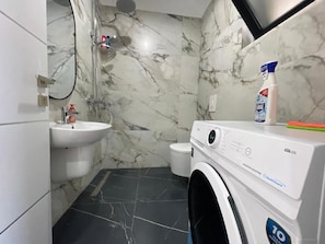 A compact bathroom with a sink, a shower, and a front-loading washing machine. - Room-sea Pearl Studios Golem - First-flo (Golem)