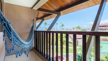Un balcon avec un hamac, des balustrades en bois et une vue sur une piscine et des palmiers.