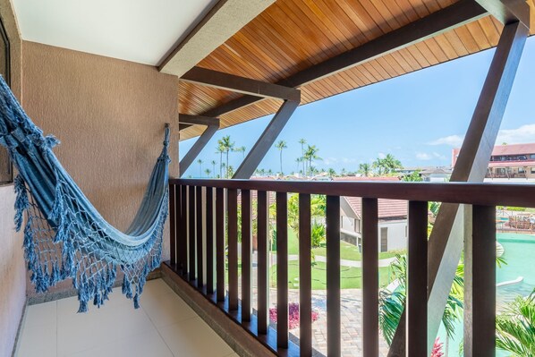 A balcony with a hammock, wooden railings, and a view of a pool and palm trees.