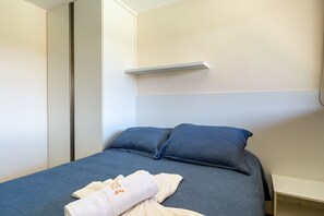 Una cama con colcha y almohadas azules, una toalla blanca y un estante blanco encima.