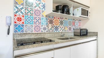 Une cuisine avec un plan de travail orné d’un revêtement mural coloré, un four à micro-ondes encastré, un grille-pain et une machine à café posés sur le plan de travail.