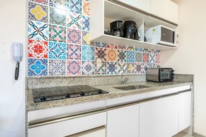 Una cocina con salpicadero de azulejos coloridos, microondas integrado, tostadora y cafetera sobre la encimera.